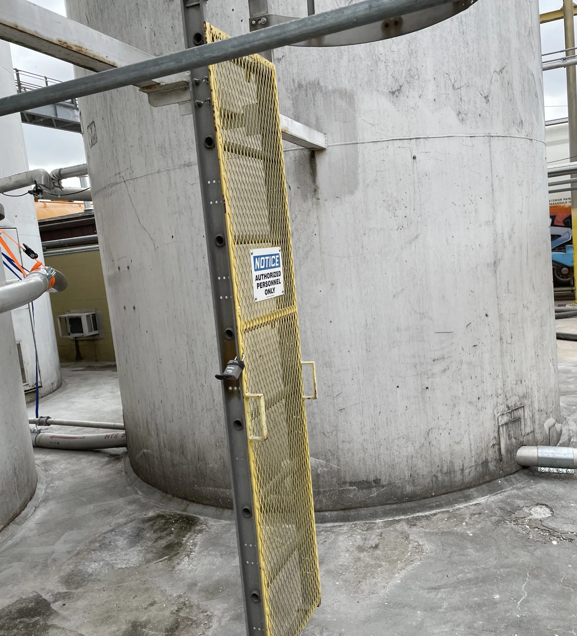 Gate with yellow mesh and notice sign reading "AUTHORIZED PERSONNEL ONLY," leading to cement silos, emphasizing safety protocols in cement silo cleaning operations.