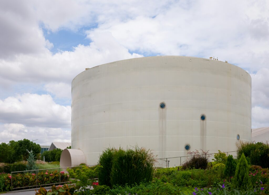 Large cylindrical storage tank surrounded by greenery, illustrating polyurea tank linings for corrosion and leak protection.