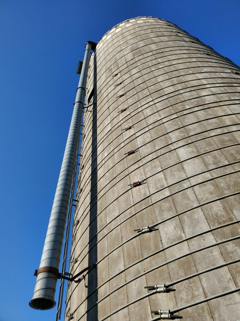 Industrial silo with a blue sky backdrop, showcasing structural features and maintenance elements relevant to silo cleaning services.