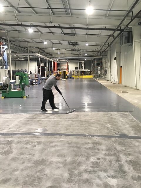 Worker applying epoxy flooring in an industrial setting, showcasing professional flooring installation for asset protection and maintenance.