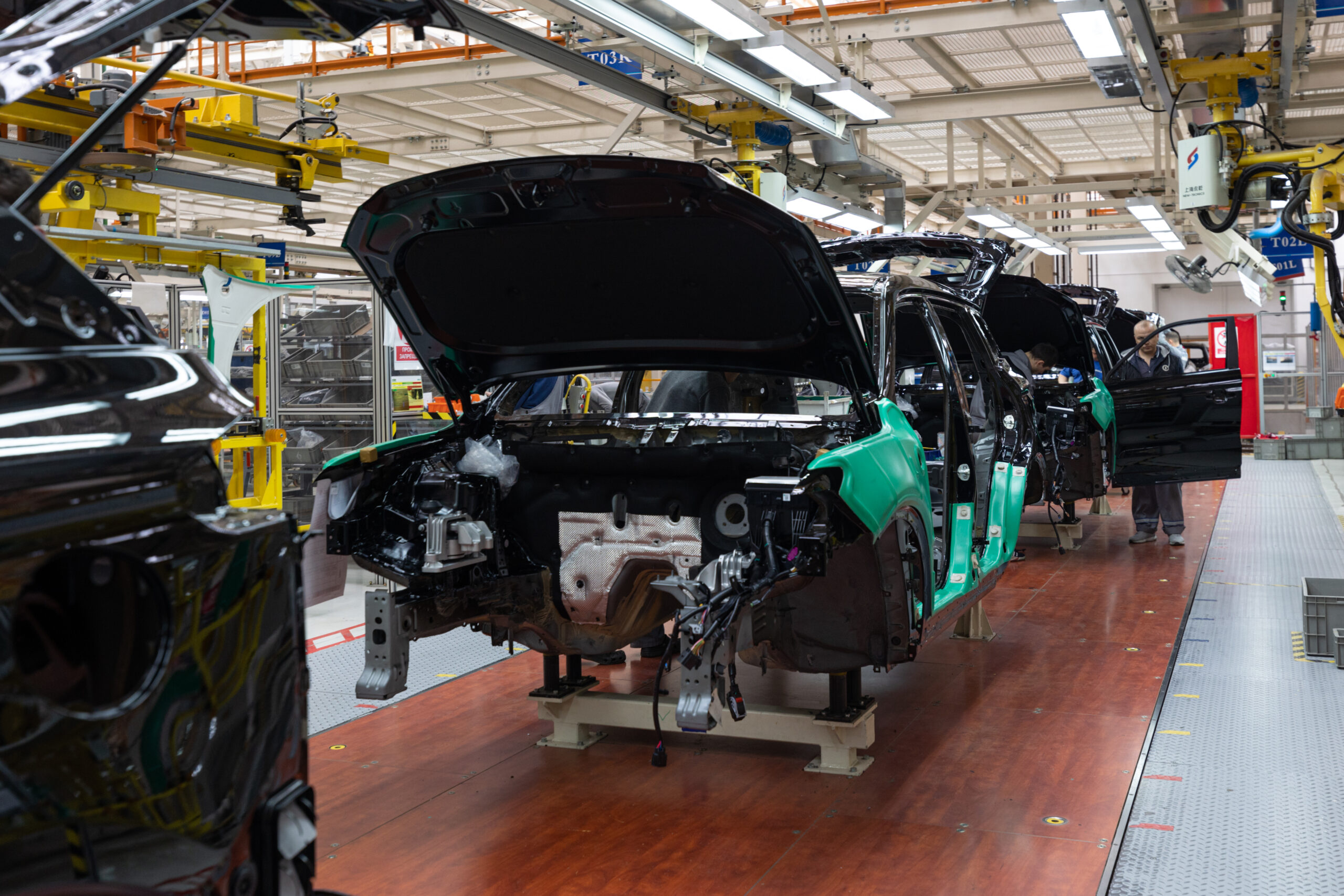 Cars on an assembly line in a modern automotive factory, featuring partially assembled car bodies with open hoods and visible components, illustrating the automotive manufacturing process.