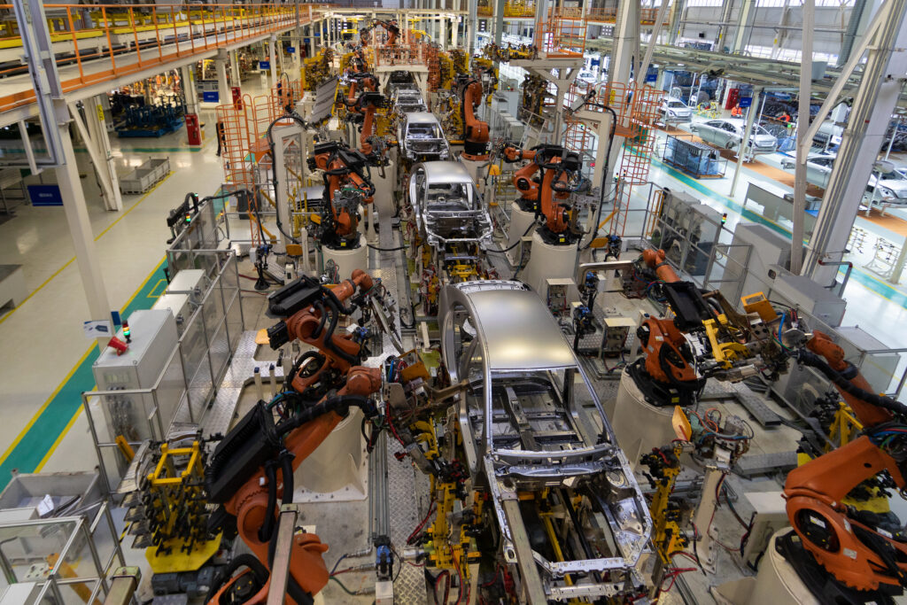 Top view of modern automotive assembly line with robotic arms working on car bodies, illustrating industrial cleaning methods like dry ice and soda blasting.