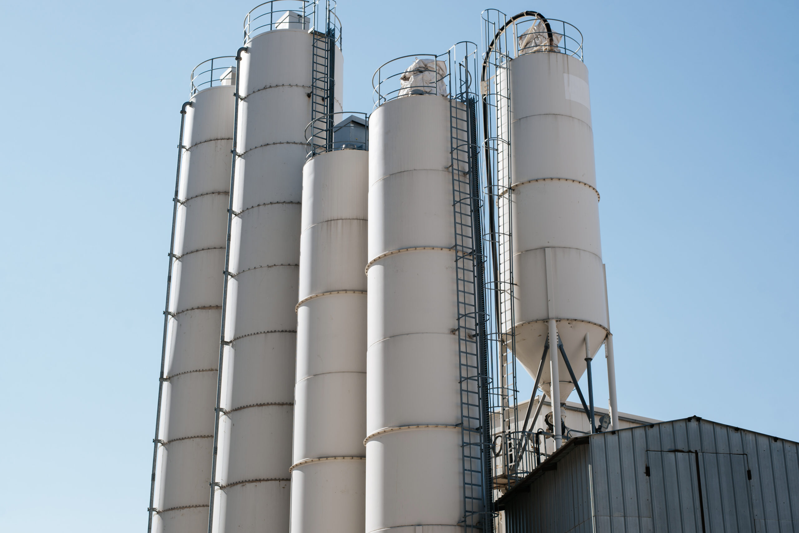 Cement silo storage tanks against a clear blue sky, illustrating industrial cleaning and maintenance practices in the cement industry.