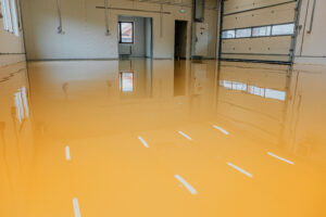 Newly installed epoxy flooring in a warehouse, showcasing a seamless, glossy orange surface with white striping, reflecting industrial efficiency and safety standards.